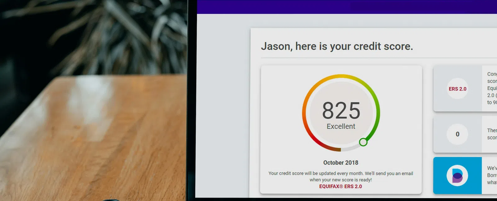 Laptop screen displays Borrowell credit score dashboard showing an excellent 825 score and a smartphone on wooden table