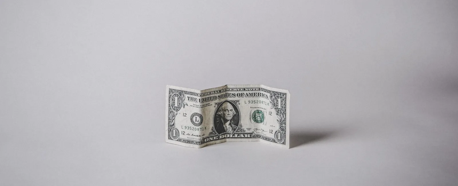 A one-dollar bill standing upright on a gray background, showcasing its detailed design and crispness.