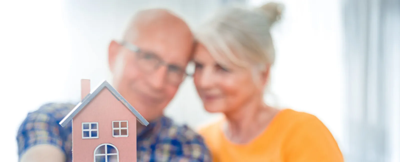 Senior couple holding a small model house symbolizing home ownership and retirement planning.
