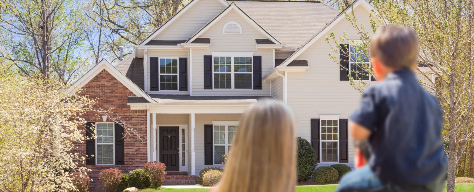 Family enjoying a sunny day in front of a beautiful suburban home with lush greenery.