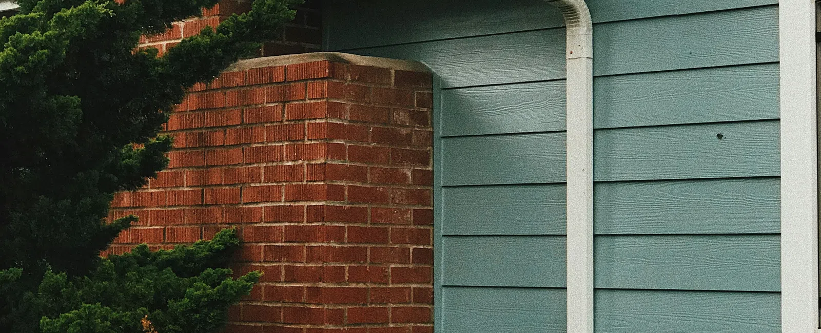Blue siding house exterior with white gutter, brick chimney, and green shrubbery in front garden