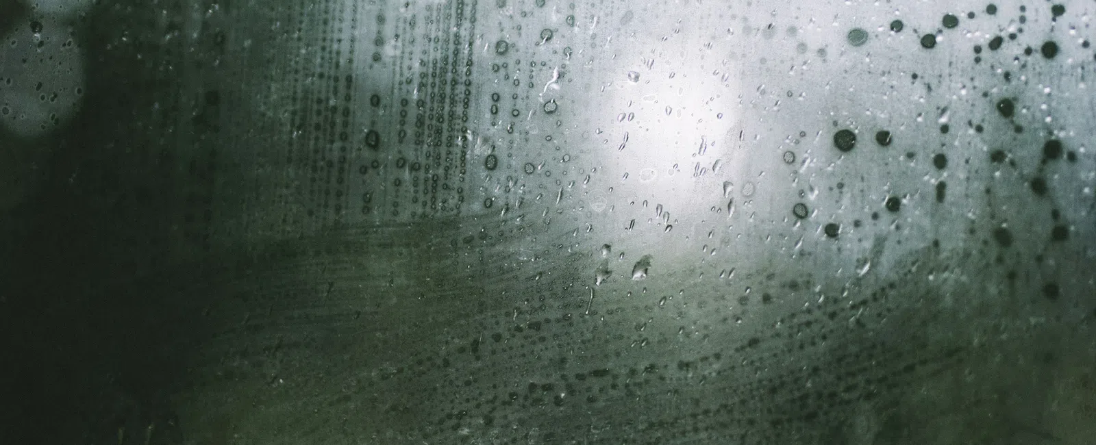 Raindrops on a foggy window with blurred green and white outdoor scenery in the background