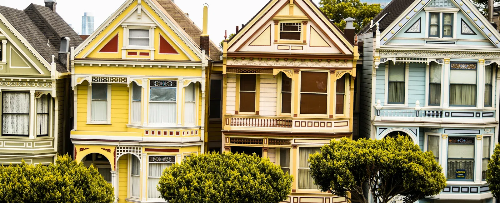 Row of colorful Victorian houses with ornamental details and trees in front on a sunny day