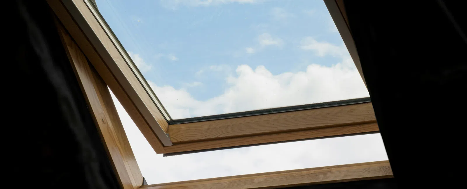 Open roof window with wooden frame showing blue sky and white clouds outside