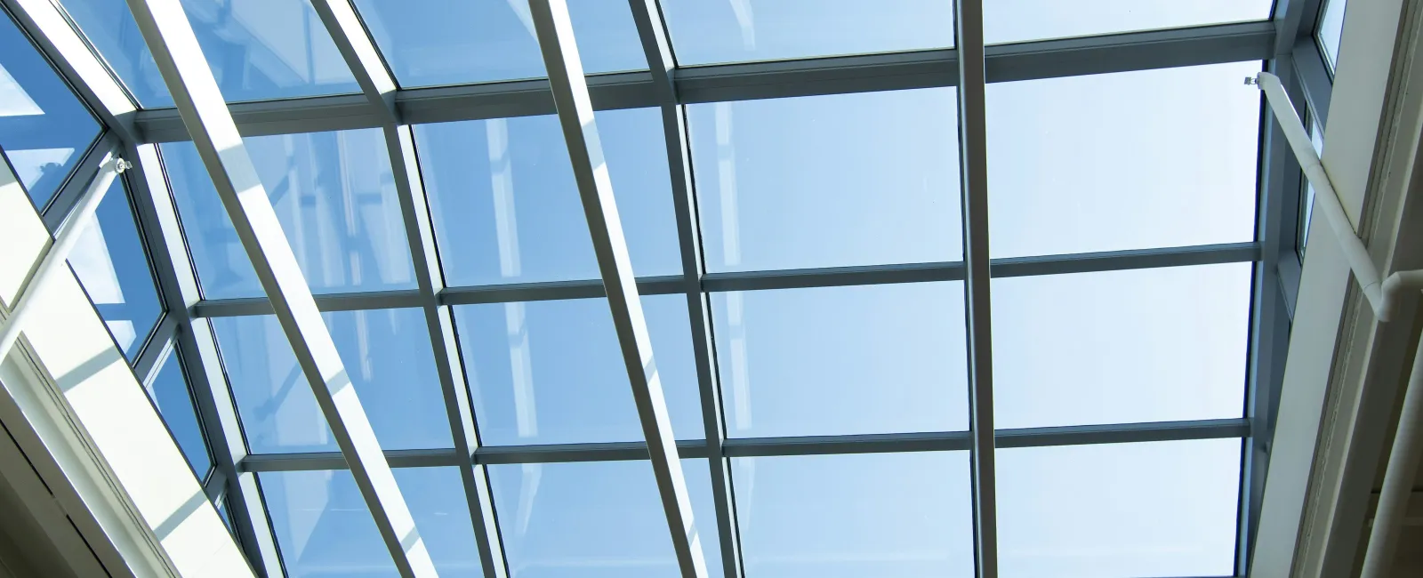 Modern ceiling skylight with large glass panels and white metal beams letting in natural daylight.