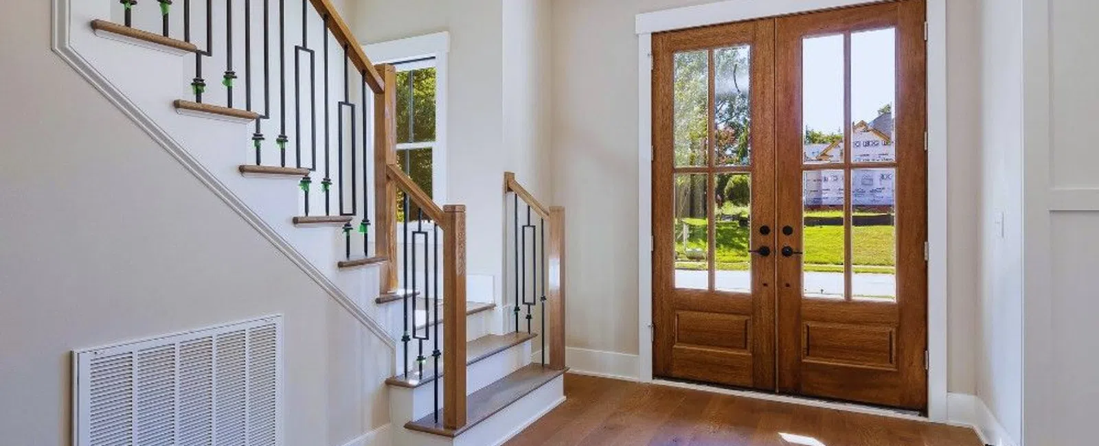 Bright modern entryway with wooden double doors, hardwood floors, and staircase with metal railings.