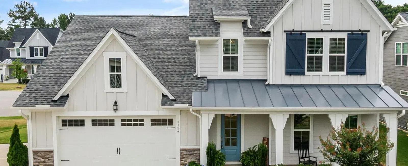 Modern two-story white house with gray roof, blue front door, garage, and landscaped front yard under a blue sky.