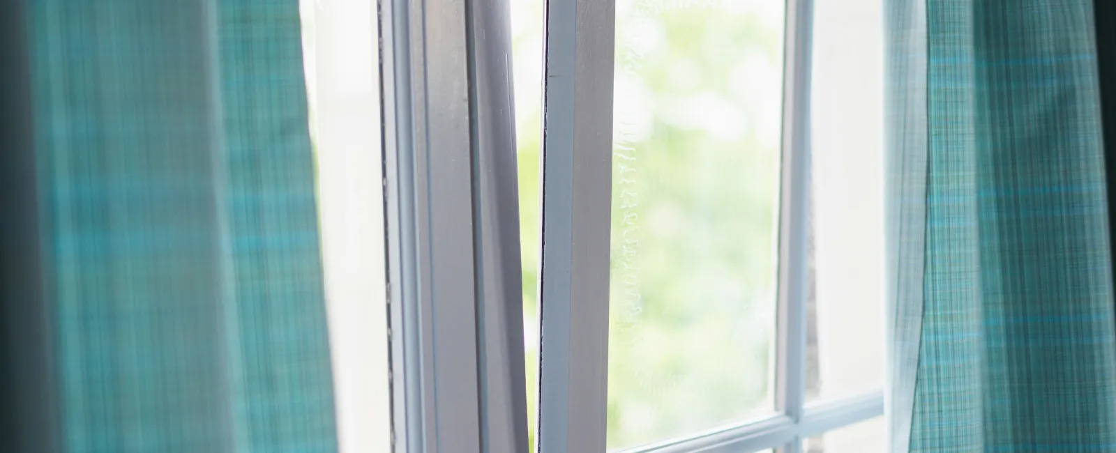 Partially open white-framed window with blue checkered curtains and soft natural light outside.