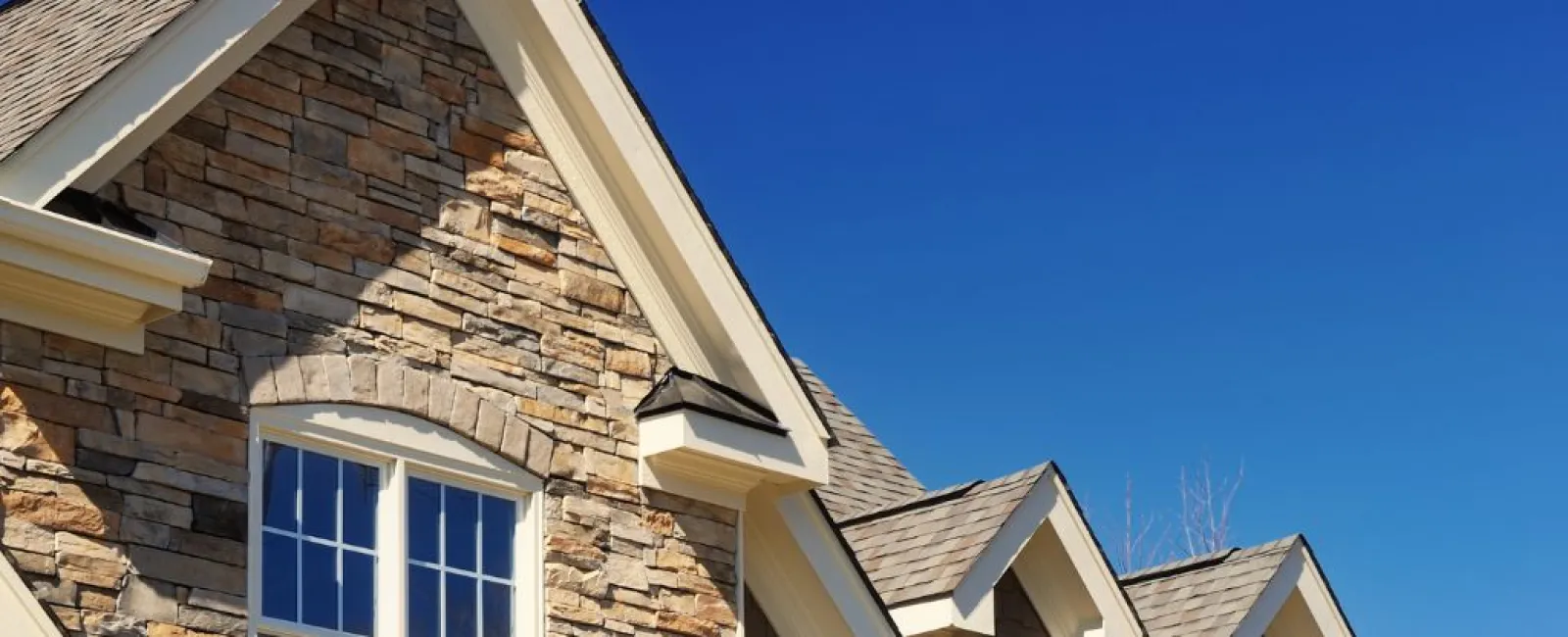 Close-up of a stone and shingle house exterior with white-trimmed windows under a clear blue sky