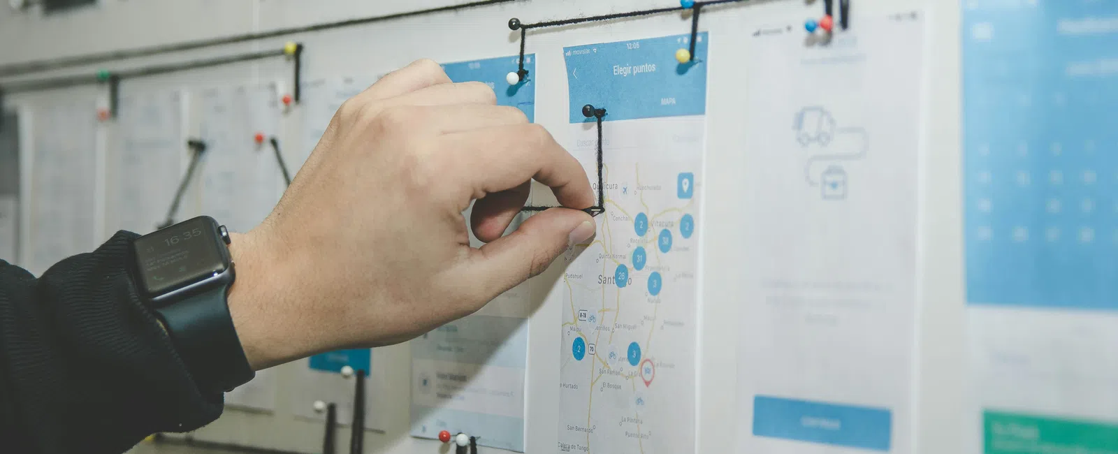 Hand pinning black string on a map connected to multiple notes on a white board for project planning.