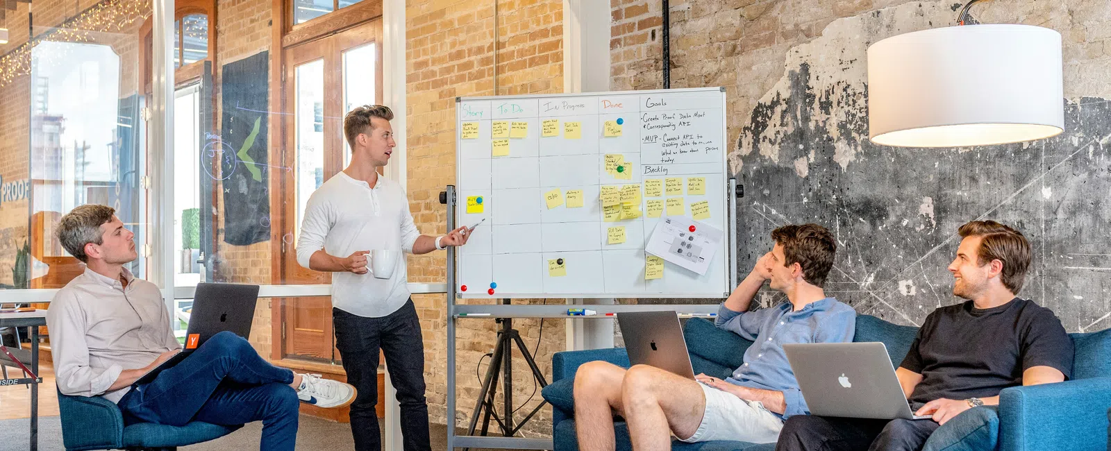 Young professionals collaborating in a modern office with laptops and a whiteboard covered in sticky notes.