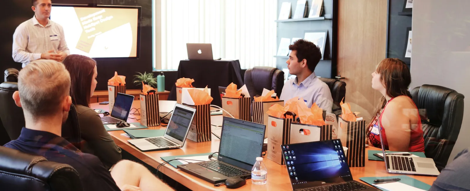 Team in a modern conference room attending a presentation with laptops and gift bags on the table