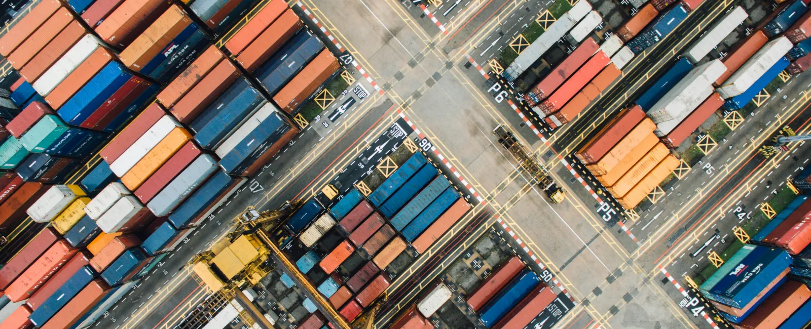 Aerial view of colorful shipping containers organized in rows at a busy cargo port terminal.