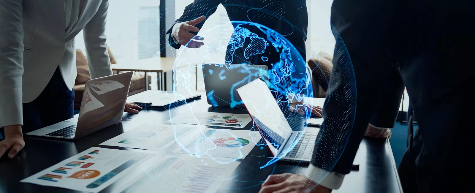 Business people discussing global strategy with digital earth hologram over conference table documents and laptops.