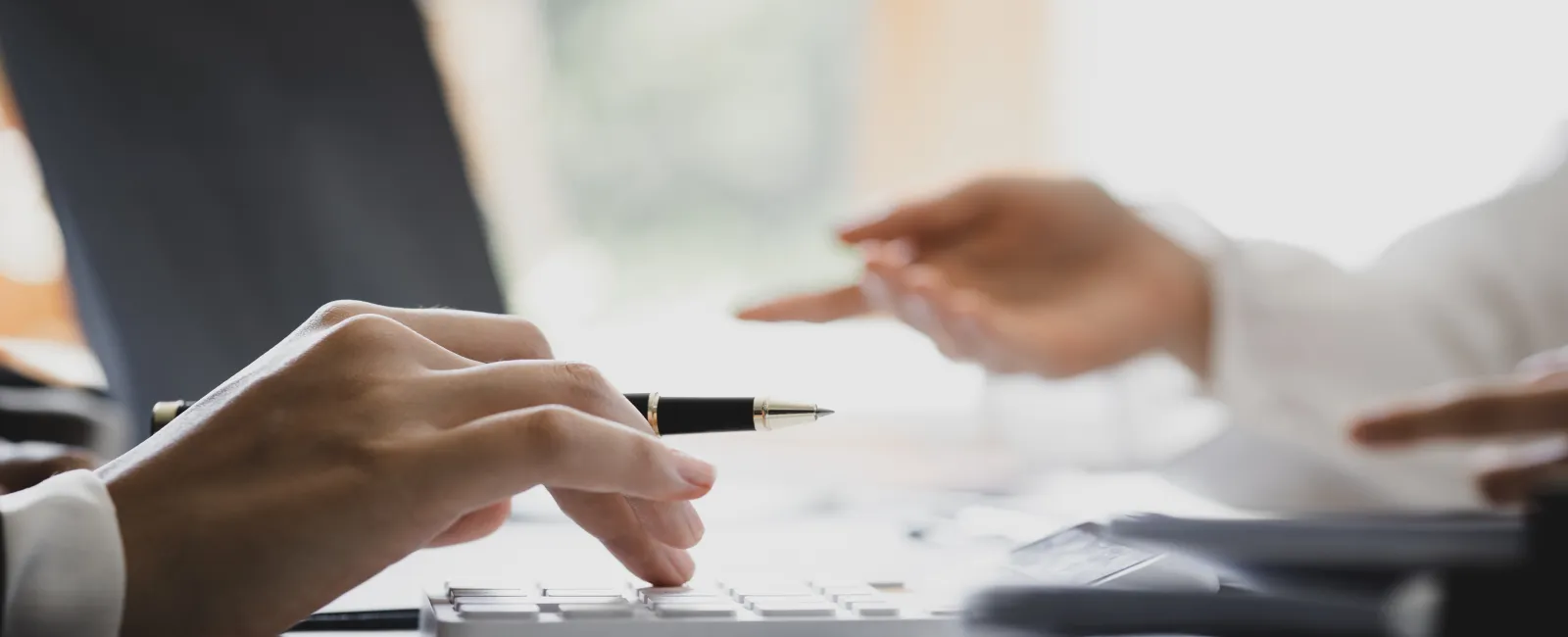 Close-up of hands using a calculator and discussing financial documents in a bright office setting