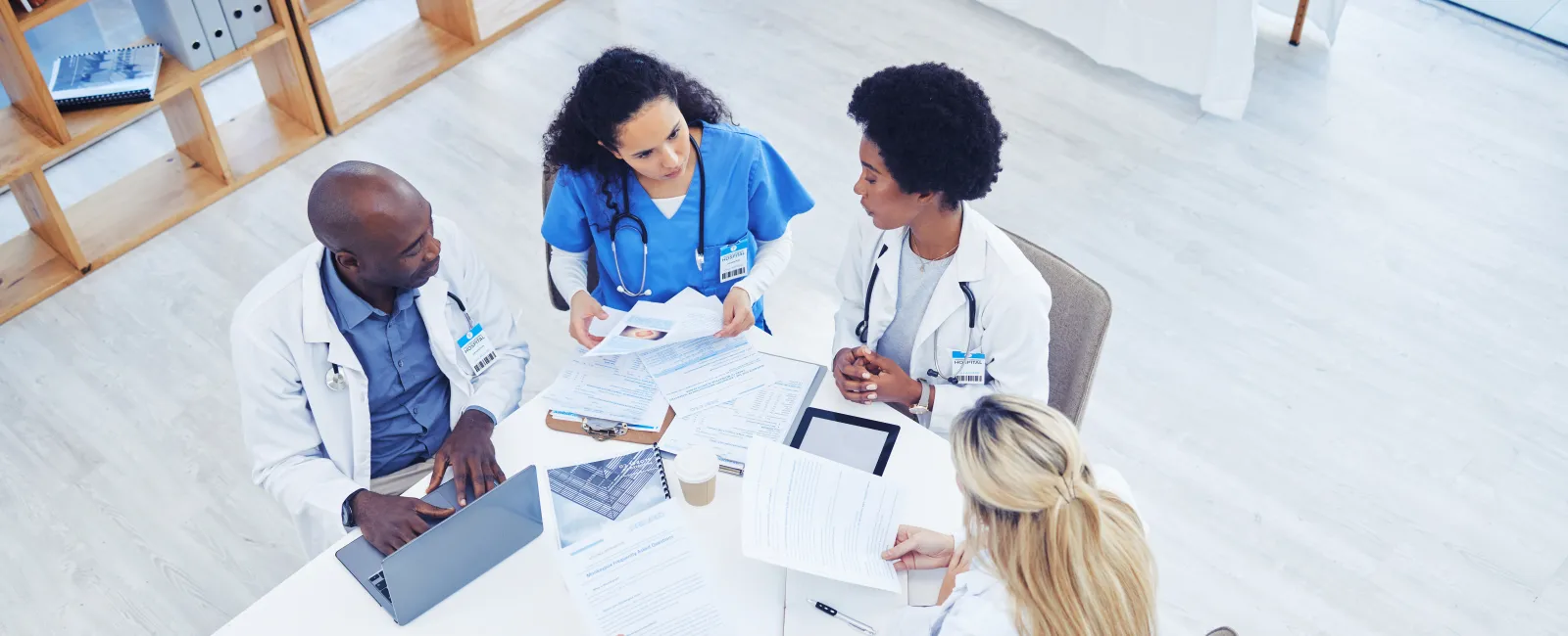 Medical team of doctors and nurses discussing patient documents around a table in a bright office.