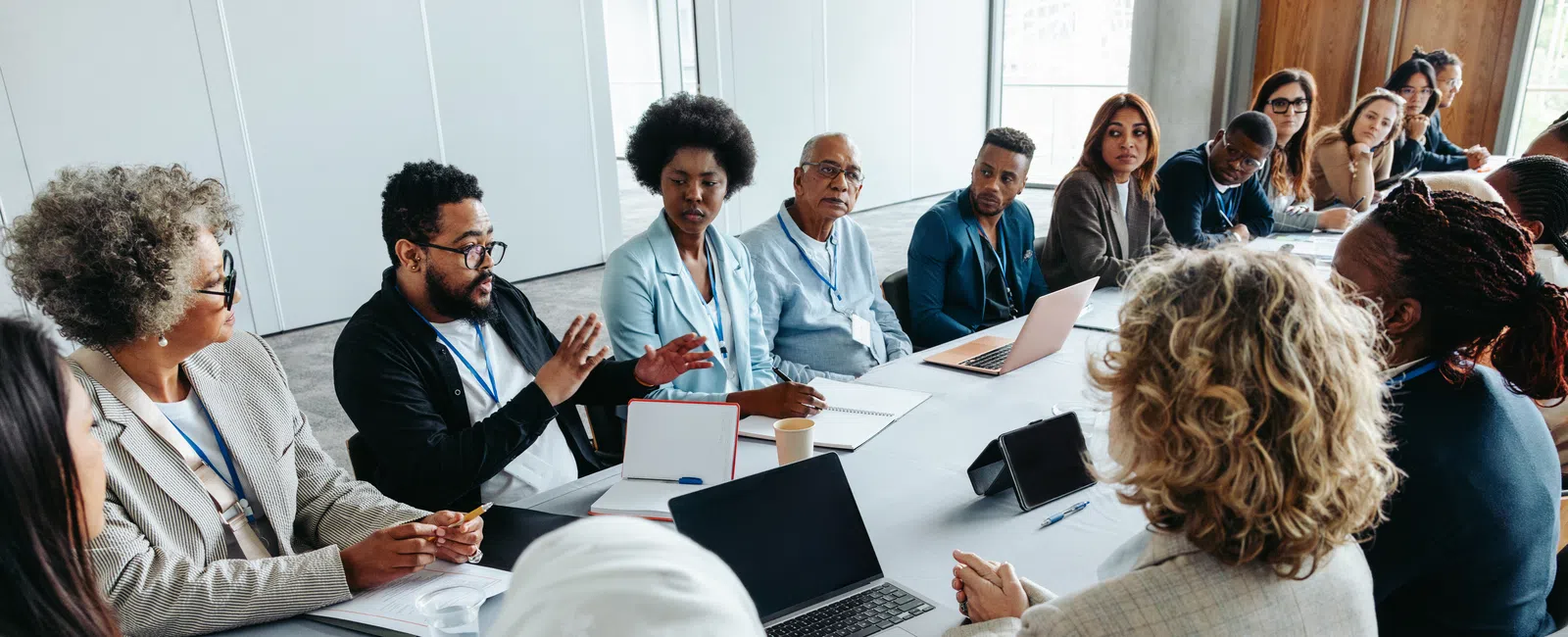 Diverse business team engaged in a discussion around a conference table with laptops and documents in a modern office.