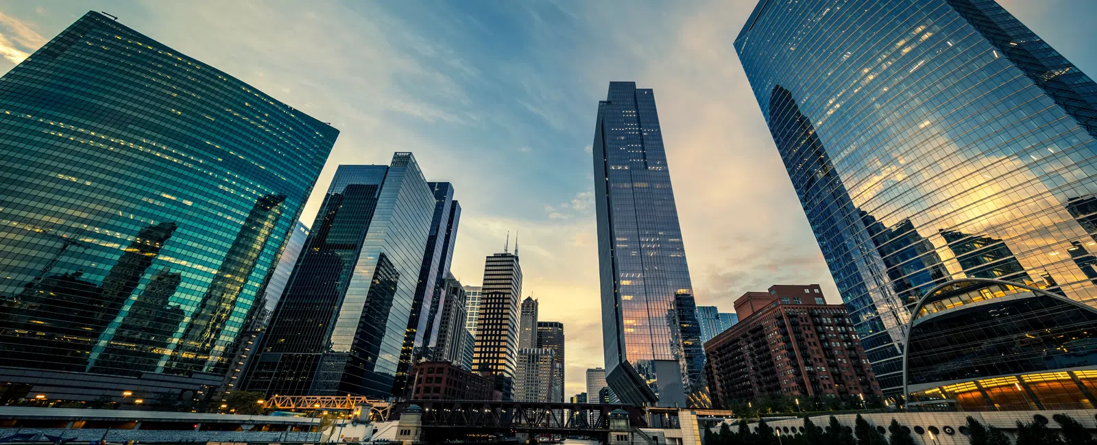 Sunset view of modern glass skyscrapers reflecting on a calm river in a vibrant cityscape.