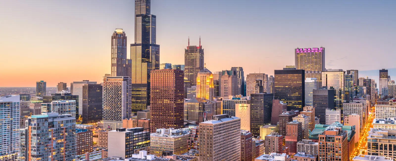 Sunset view of Chicago skyline featuring Willis Tower and city buildings with warm lighting and clear sky.