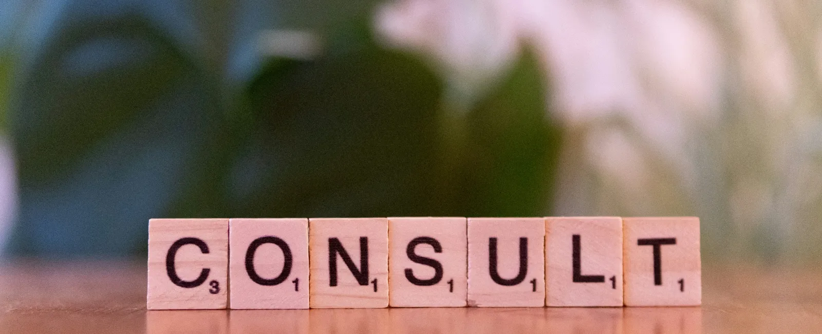 Wooden Scrabble tiles spelling CONSULT on a reflective surface with green blurred background