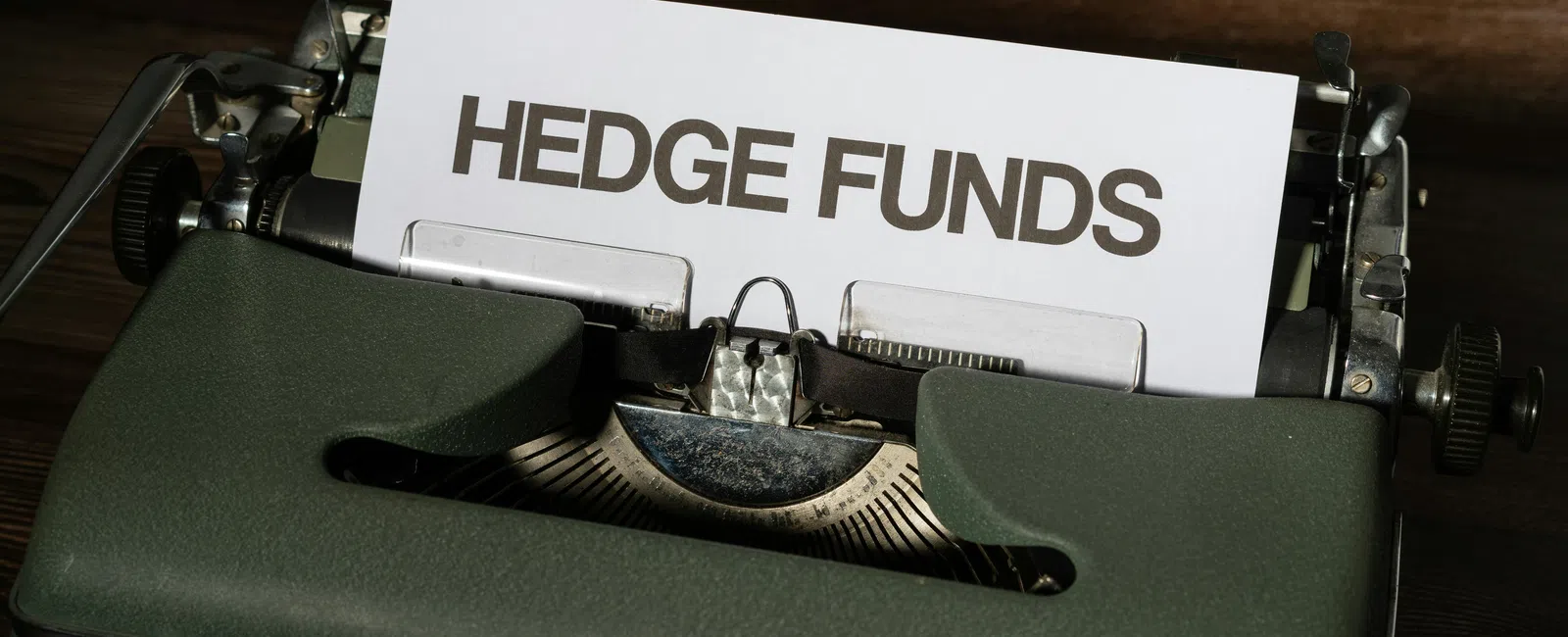 Old typewriter with paper displaying the words Hedge Funds on a wooden surface background.