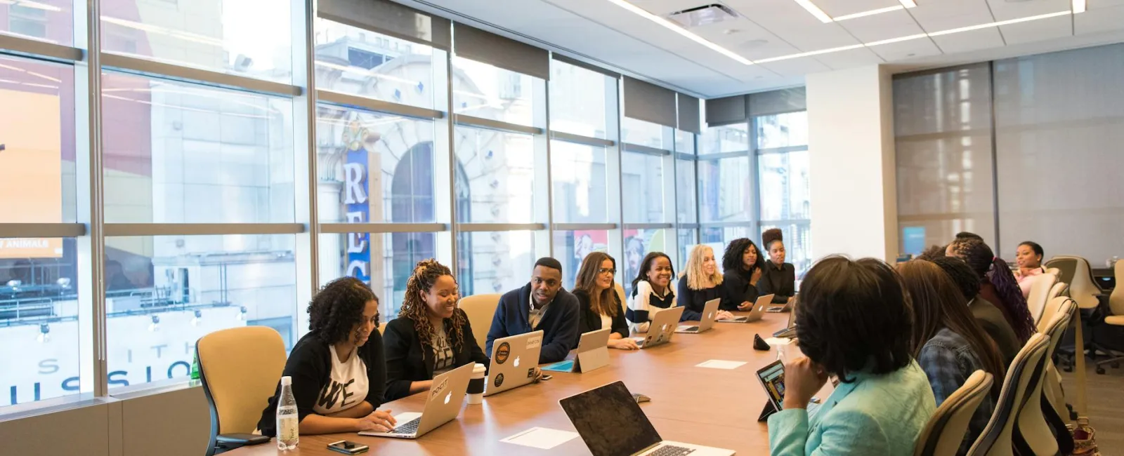 Diverse group of professionals collaborating around a large conference table with laptops in a modern office.