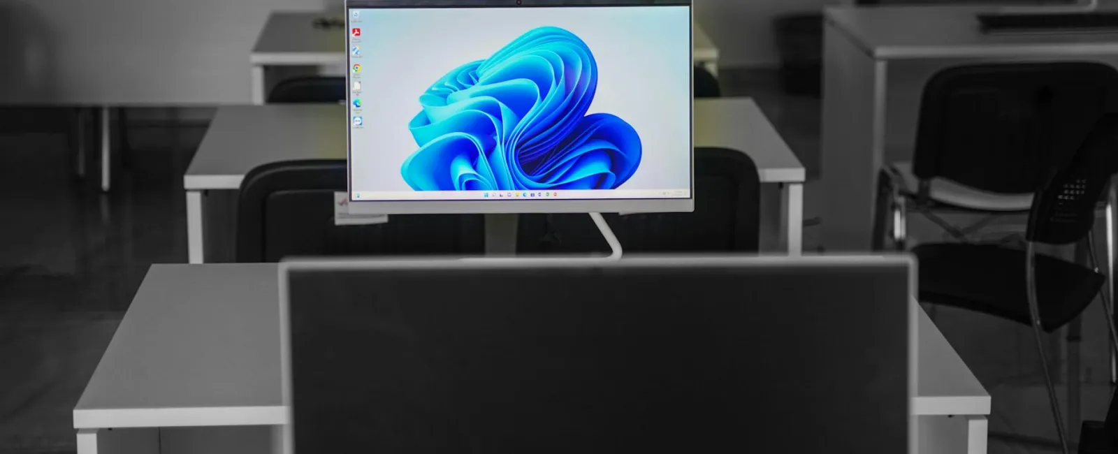 Modern office with multiple desks and computers, one screen displaying Windows 11 desktop background.