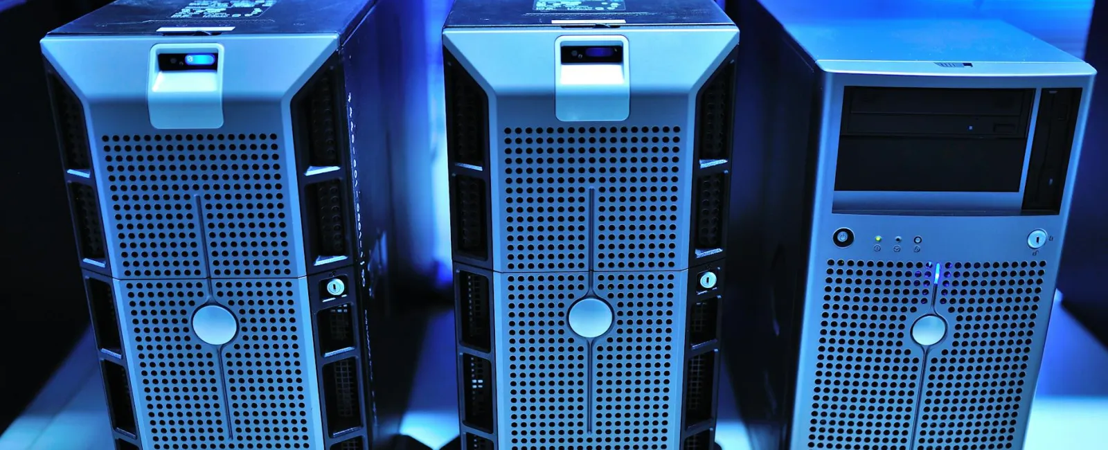Three metal computer servers with ventilation grids placed on a shelf in a blue-lit data center environment.