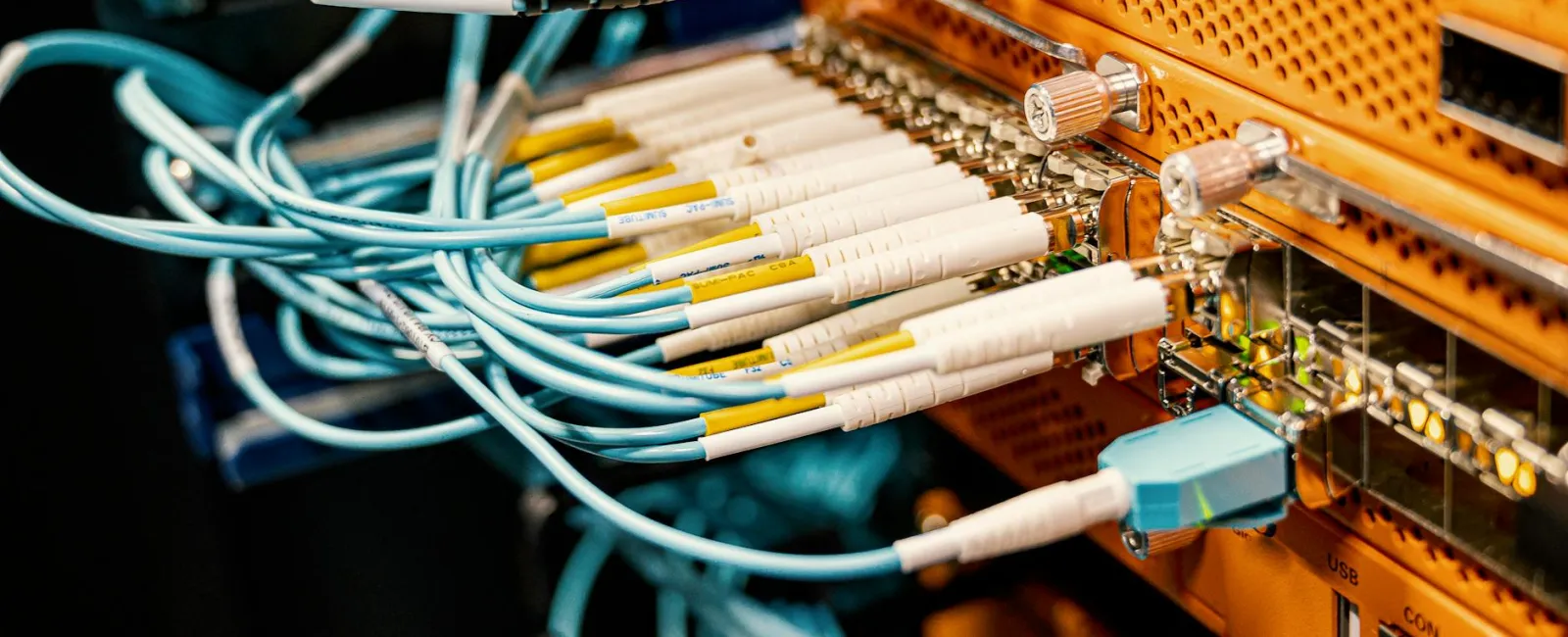 Close-up of fiber optic cables connected to an orange network switch in a server room setup.