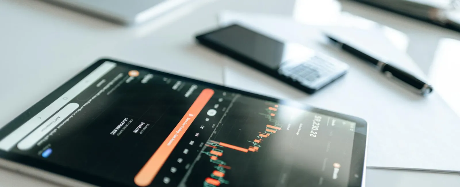 Tablet displaying financial chart with bar graphs on desk alongside laptop, smartphone, and pen.