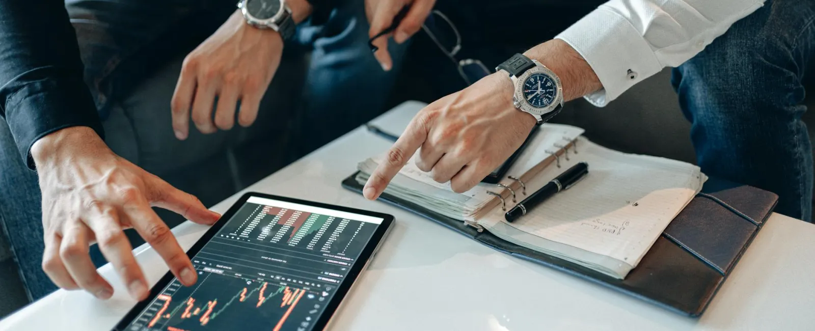 Two professionals analyzing financial data on a tablet with charts and notes on a table during a meeting