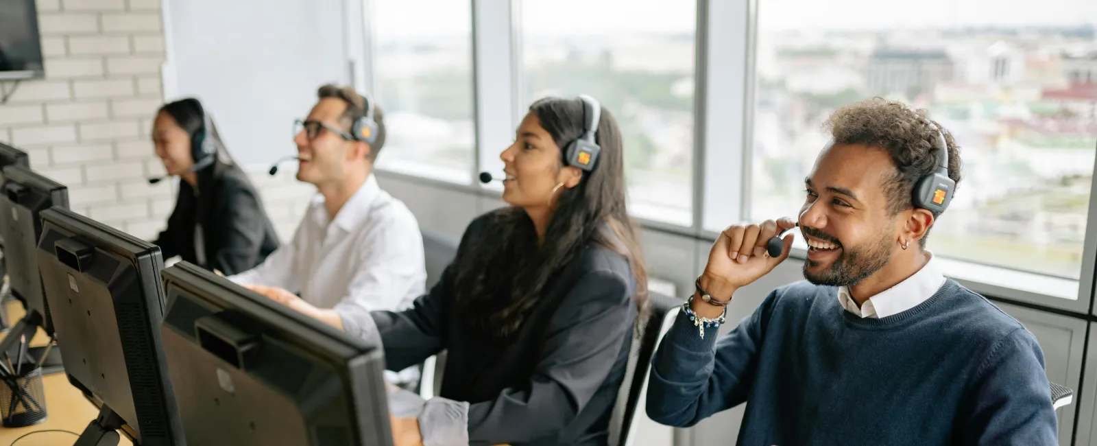 Customer service team wearing headsets and working on computers in a modern office with large windows.