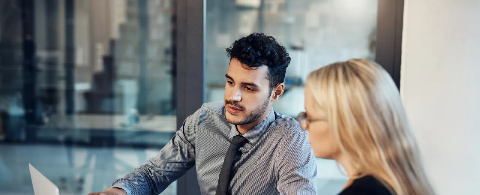 Young professionals discussing work on a laptop in a modern office setting during a meeting