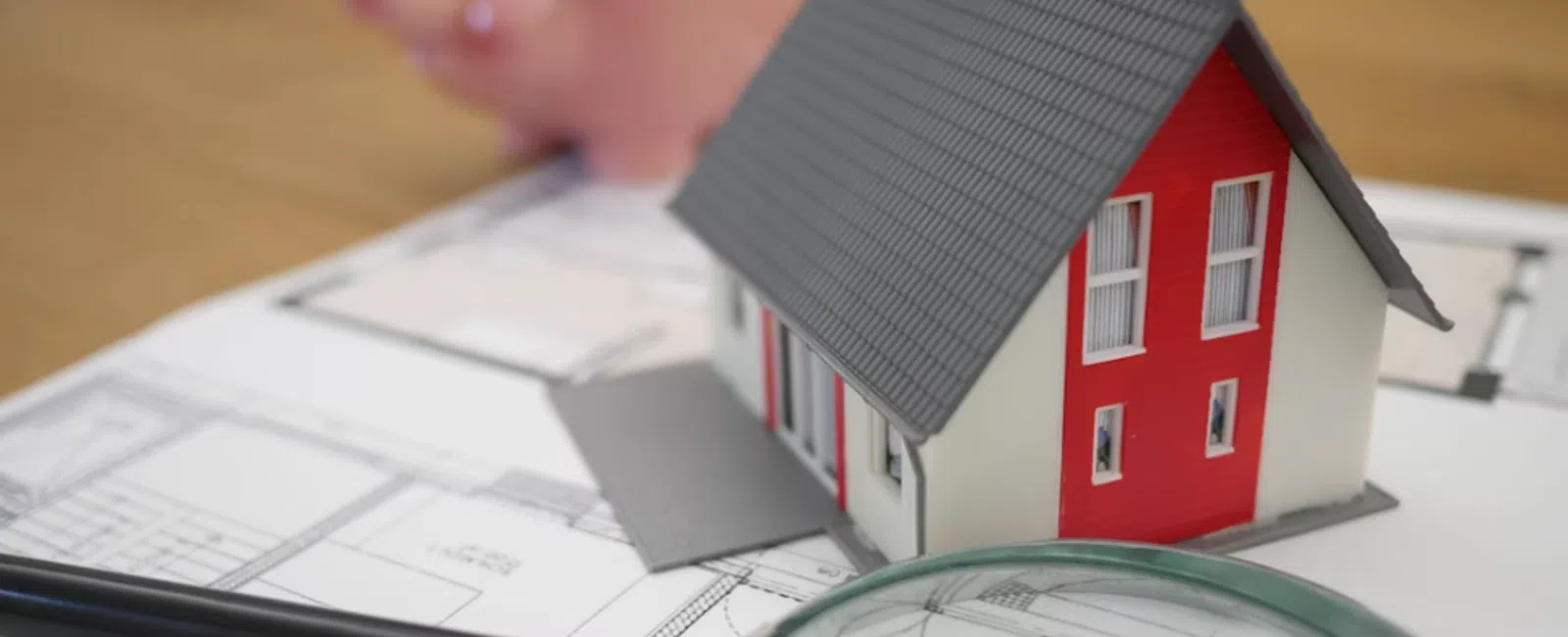Model house on architectural blueprints with magnifying glass and piggy bank for home planning finance