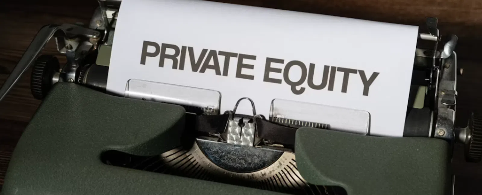 Vintage typewriter with paper displaying the words Private Equity on a wooden surface.