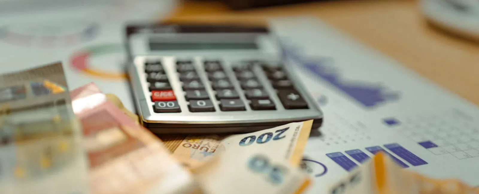 Calculator on financial documents with various euro banknotes spread out on the table