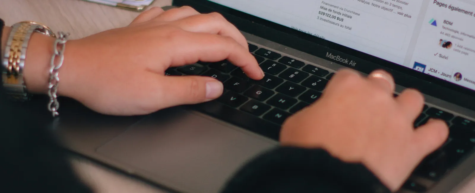Person typing on a MacBook Air laptop viewing a LinkedIn page for Swello social media management tool.
