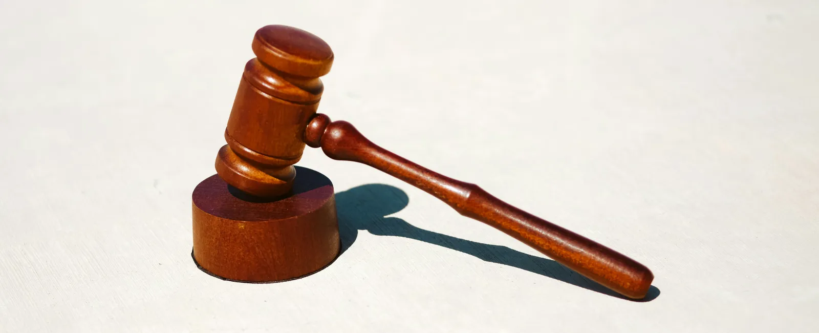 Wooden judge gavel resting on a sound block casting a shadow on a white background.