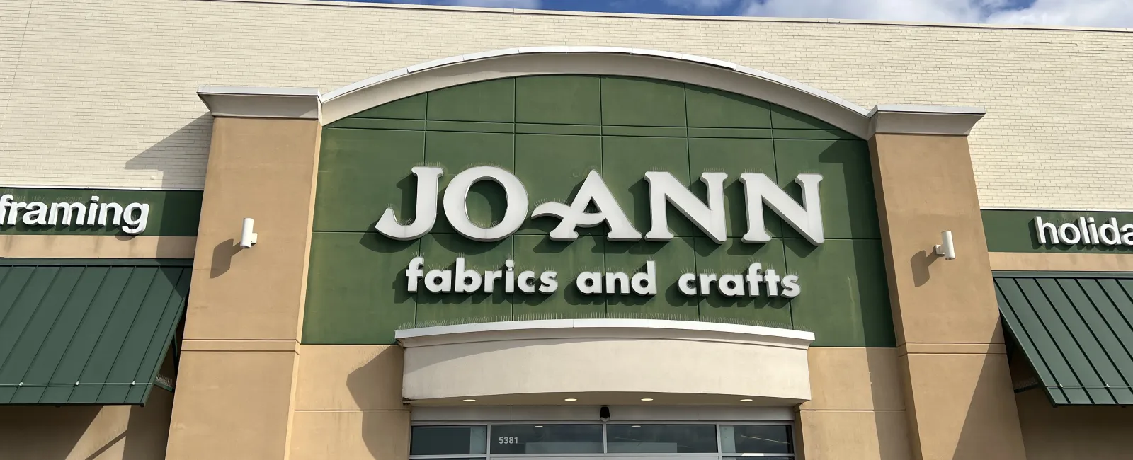 Front entrance of JOANN fabrics and crafts store with green and beige exterior under a blue sky