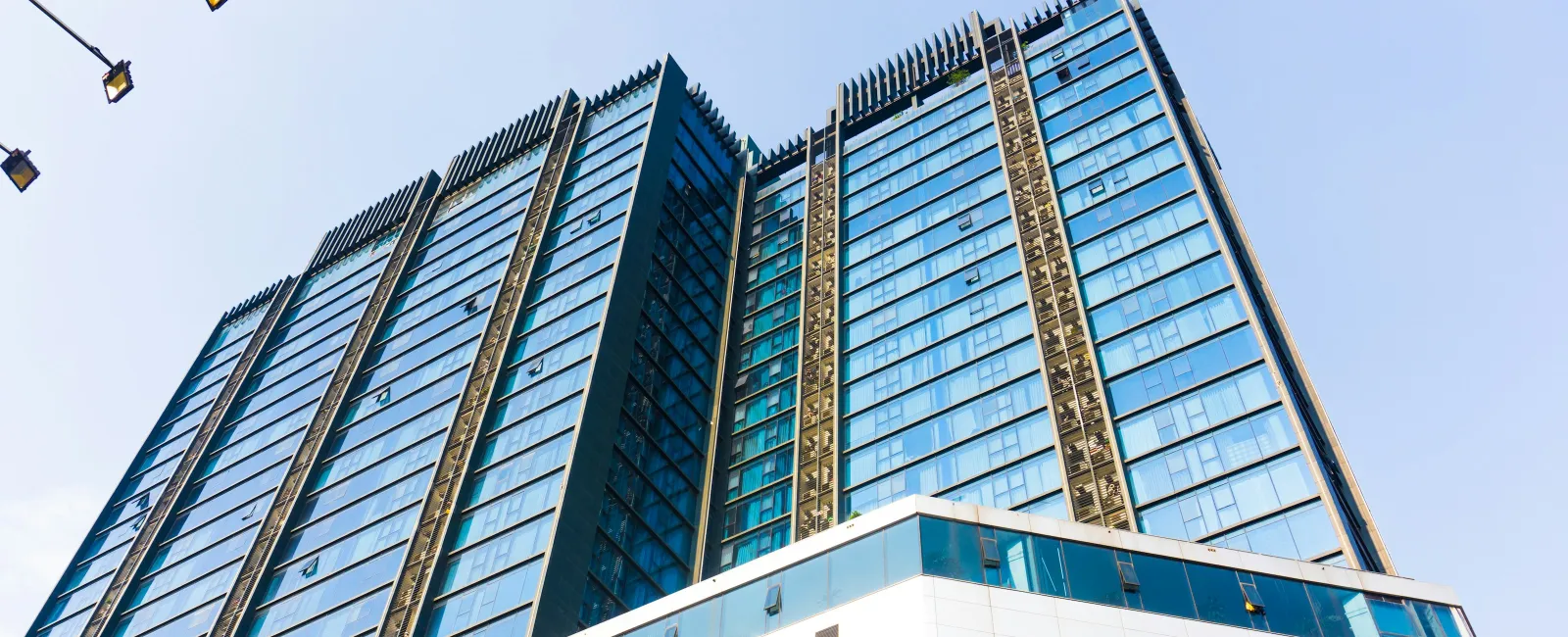 Modern glass skyscraper with blue windows and white base under clear sky, viewed from below.