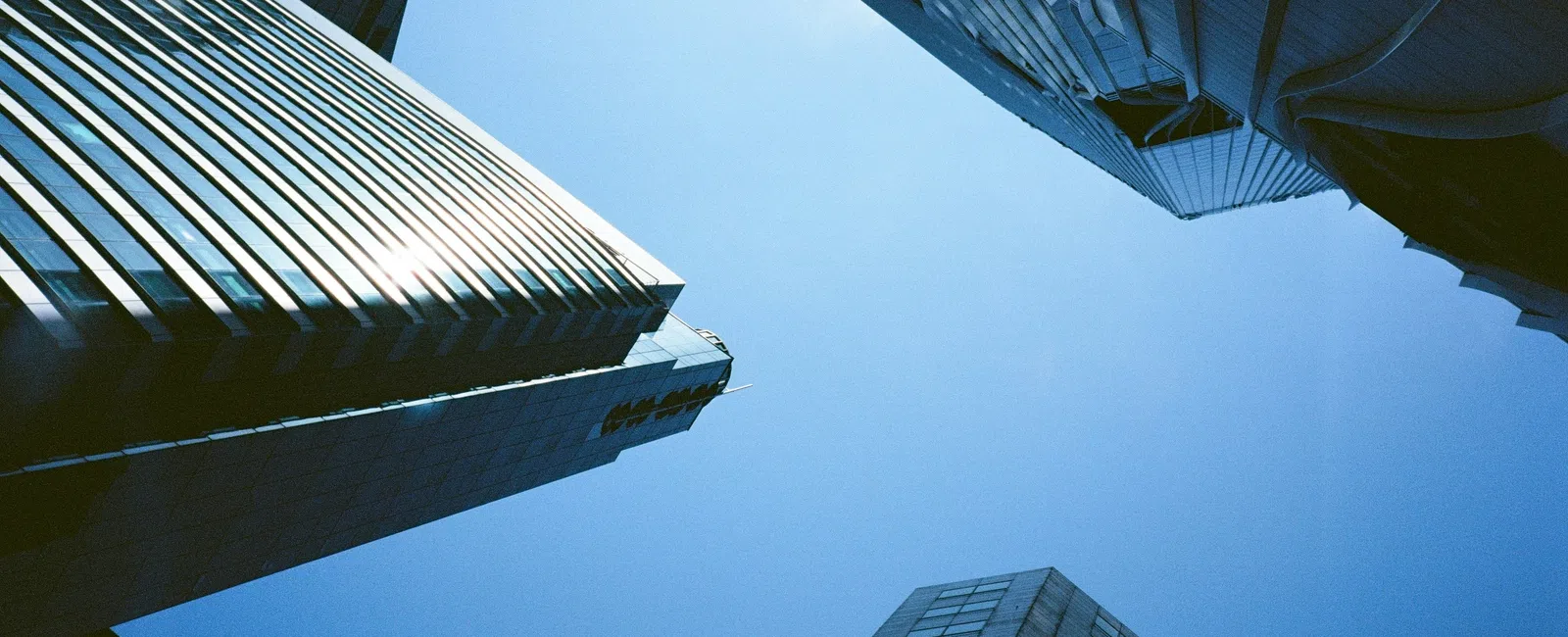 Modern glass skyscrapers reflecting sunlight under a clear blue sky from a low angle view.