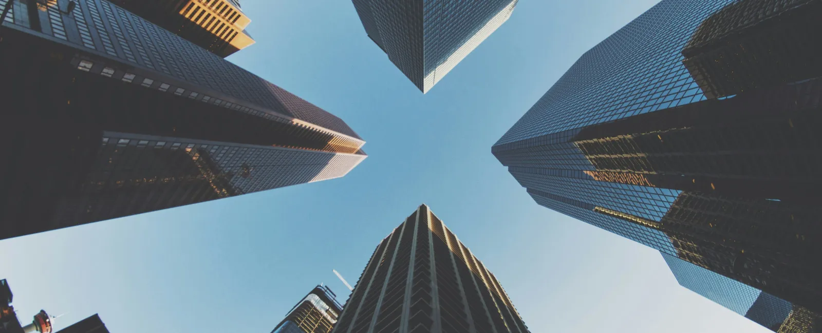 Skyscrapers converging towards the sky in an urban cityscape with clear blue sky background.
