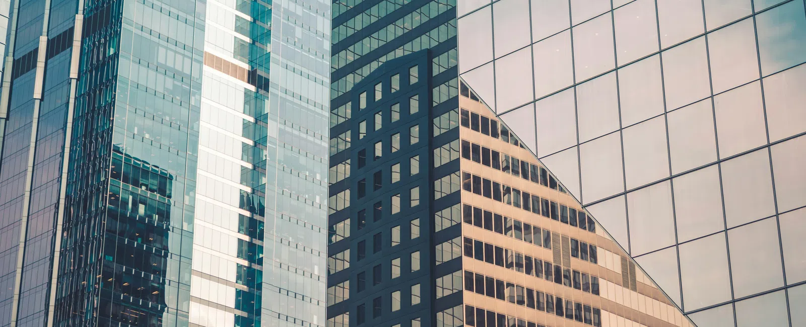 Modern glass skyscrapers with reflective surfaces showing urban architectural patterns and blue sky.