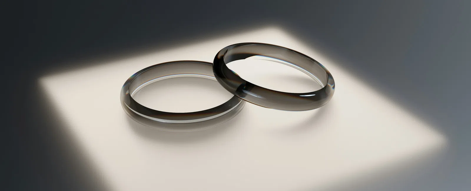 Two silver wedding rings casting soft shadows on a smooth surface with focused light.