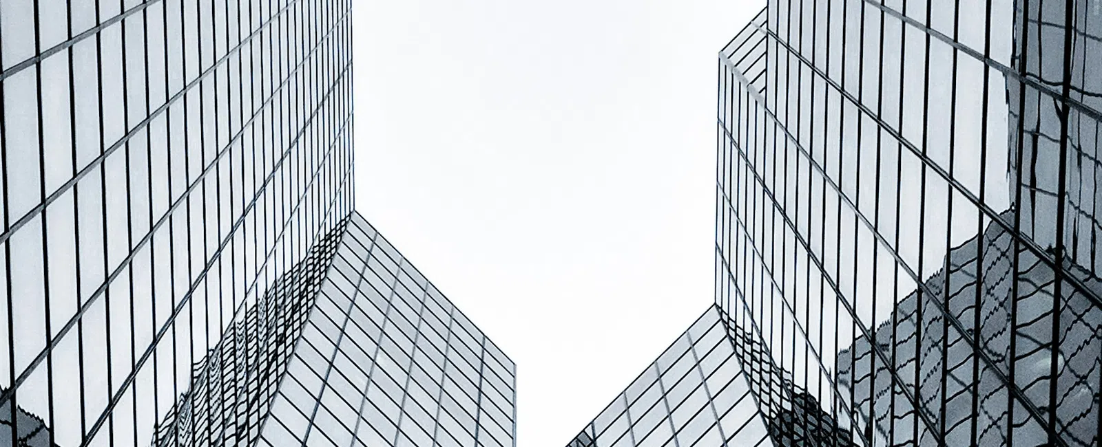 Perspective view of tall reflective glass skyscrapers converging under an overcast sky in an urban setting