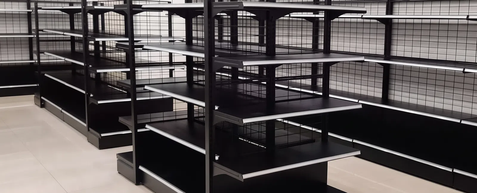 Empty black metal store shelves with grid panels in a clean, well-lit retail space with tiled floors.