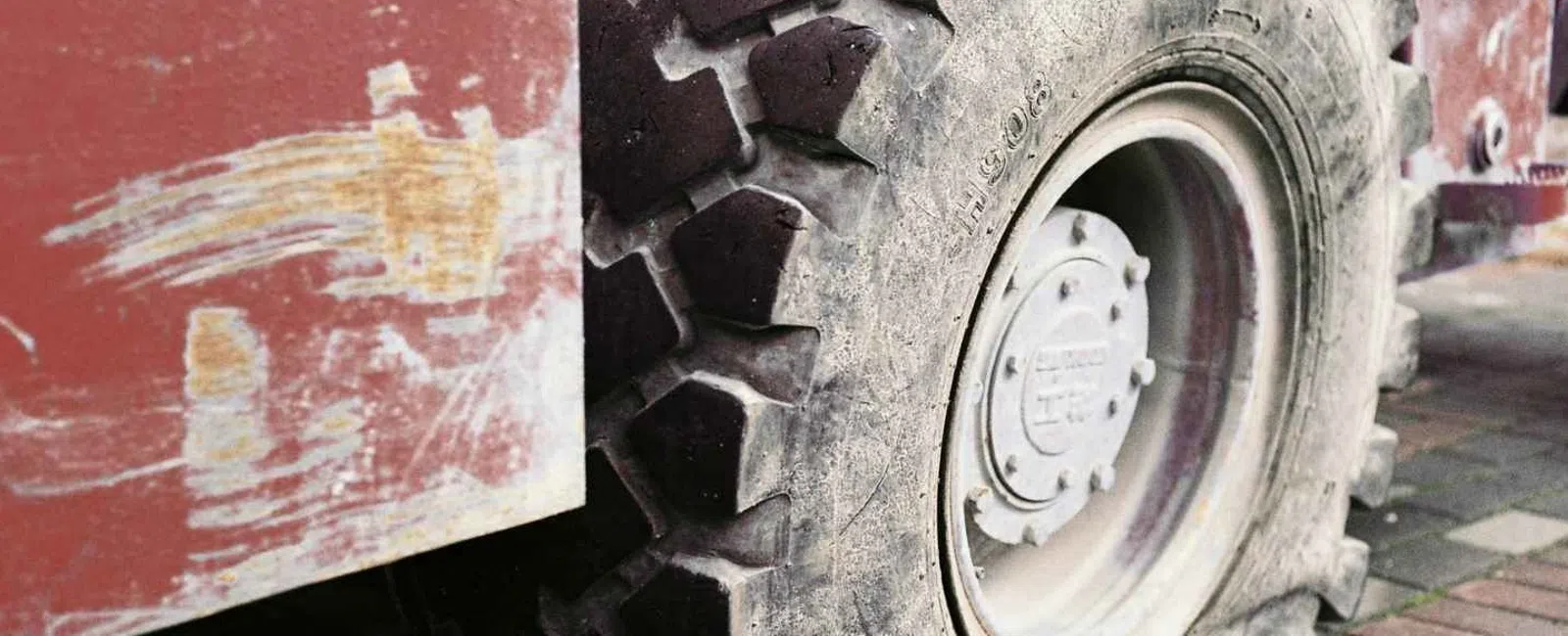 Close-up of a large flat tire on a rugged industrial vehicle with a worn red body and brick pavement.