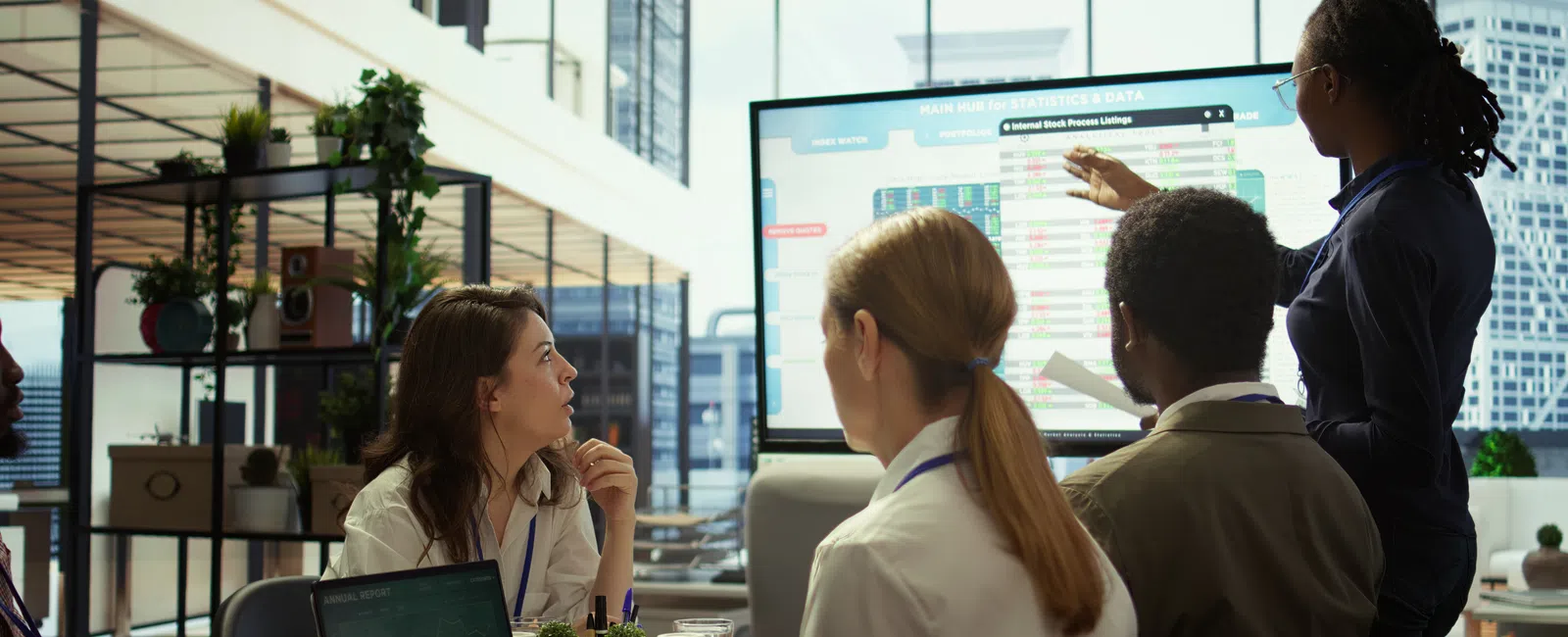 Team meeting in modern office with diverse professionals discussing data on large screen display.