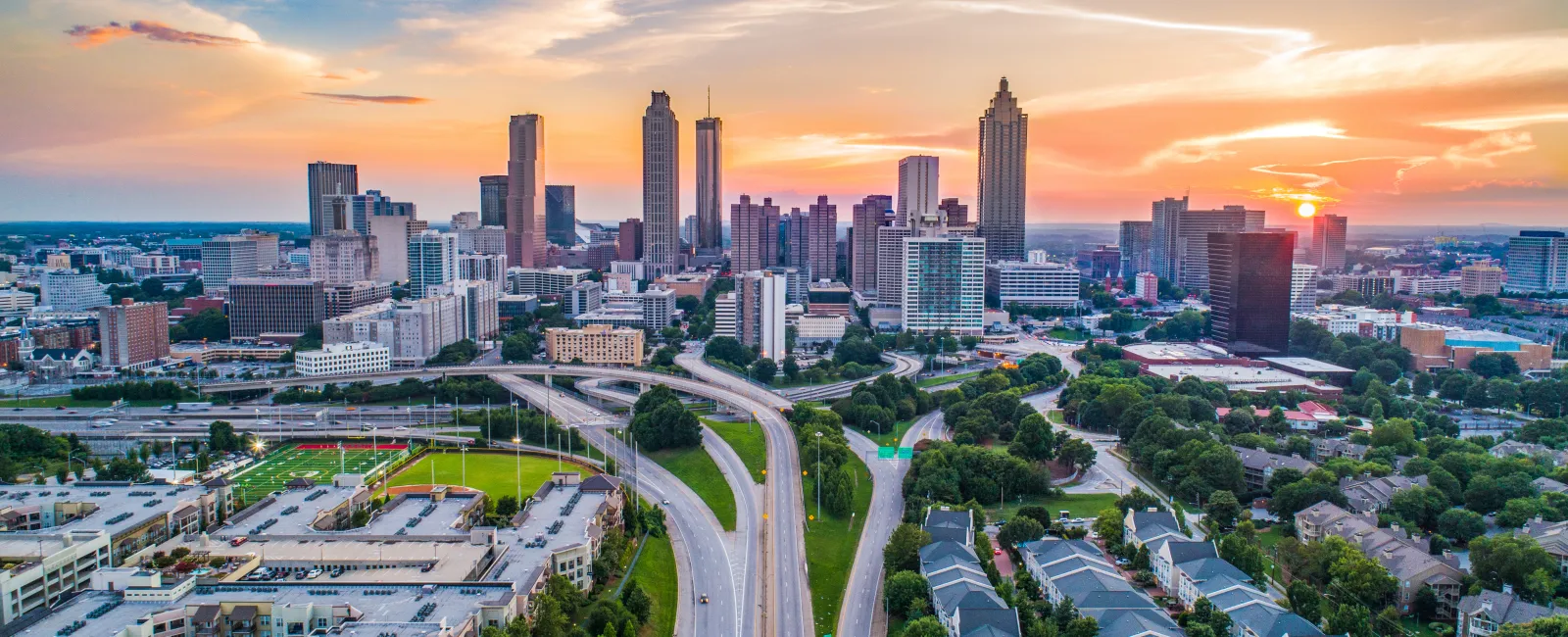 Sunset over Atlanta city skyline with highways, green spaces, and residential buildings in clear sky.