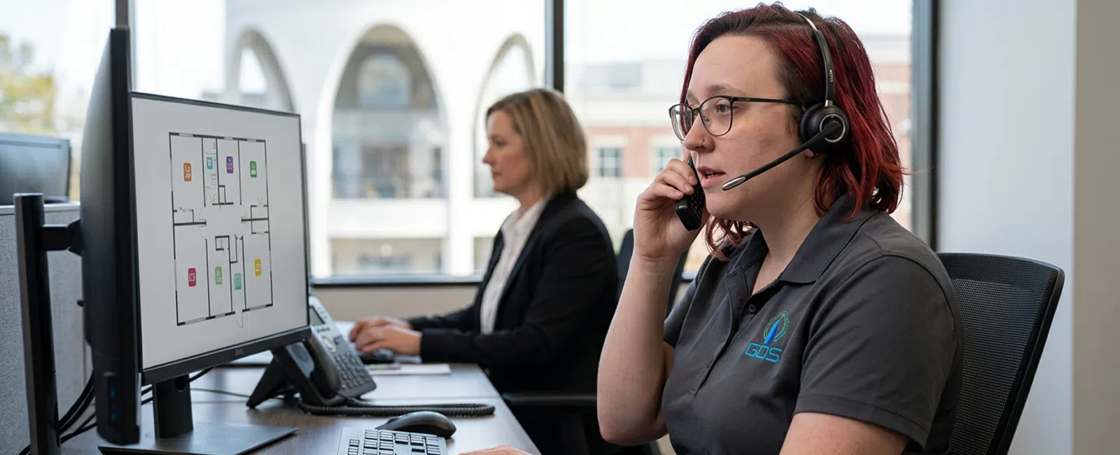 A focused GDS dispatcher in a charcoal polo and headset supports a Carmel property manager by phone at a quiet help desk, with the